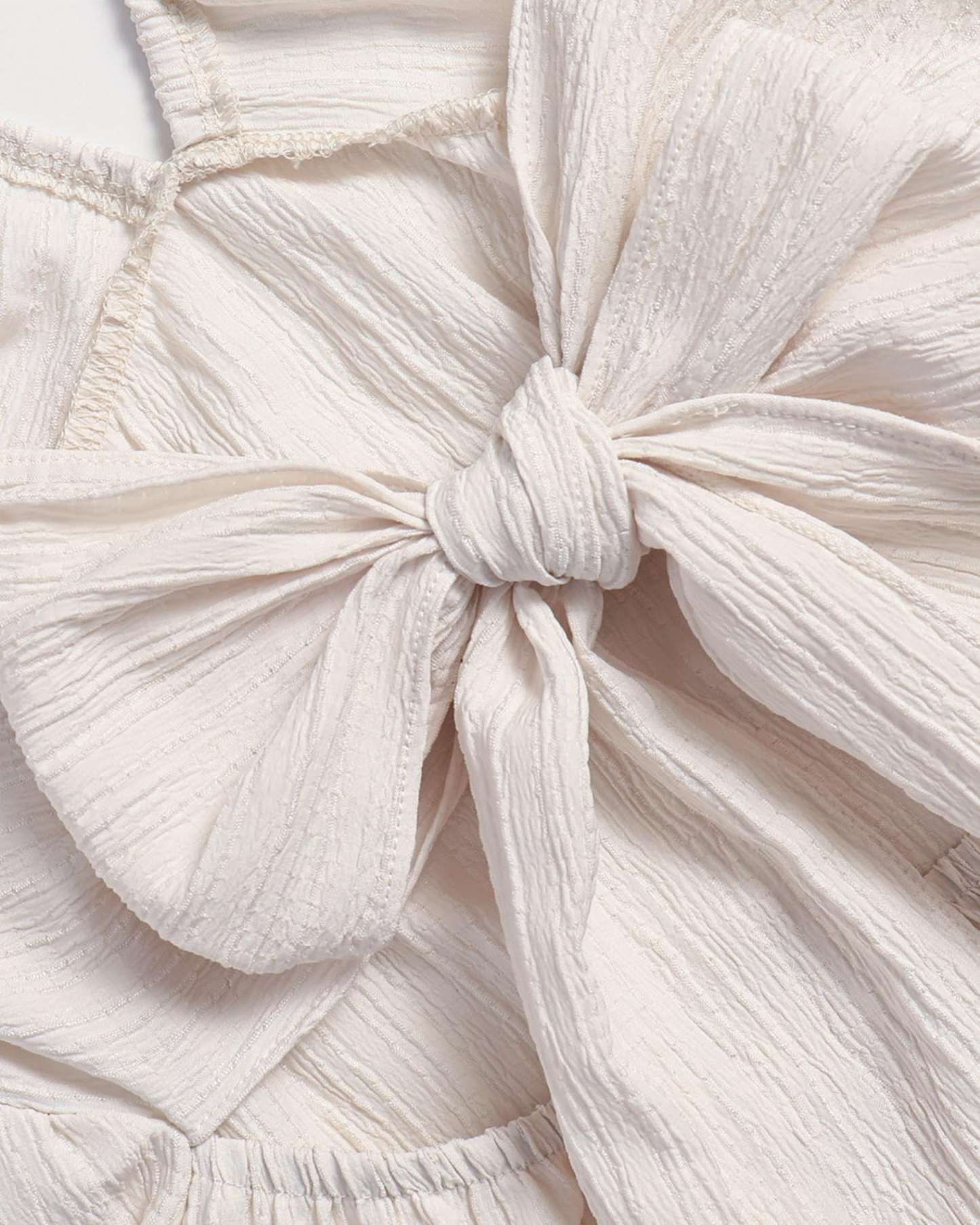 Detail of the Alva back sash knotted into a soft bow in cream crinkle fabric