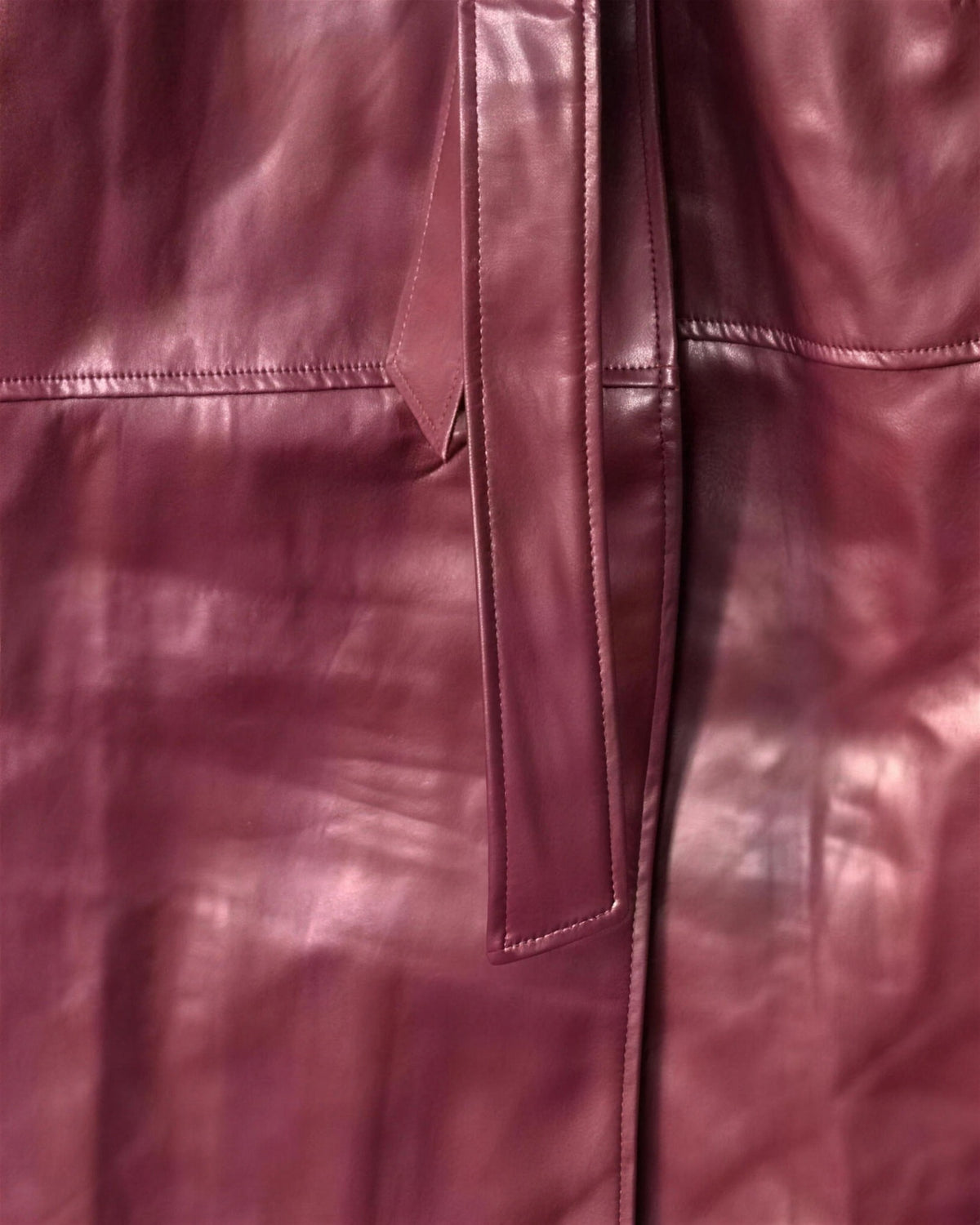 Macro of the Alya burgundy faux leather, showing the gloss, the stitched seam and the tie belt end