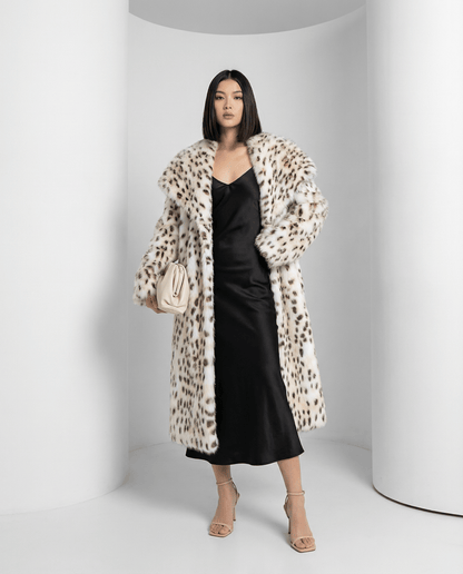 Snow-leopard faux-fur coat in a three-quarter turn over a black slip dress, cream clutch in hand