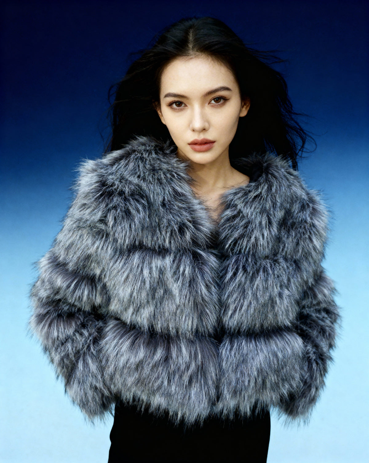 Cropped glacier grey faux-fur jacket shot waist up on a blue backdrop, collarless neckline