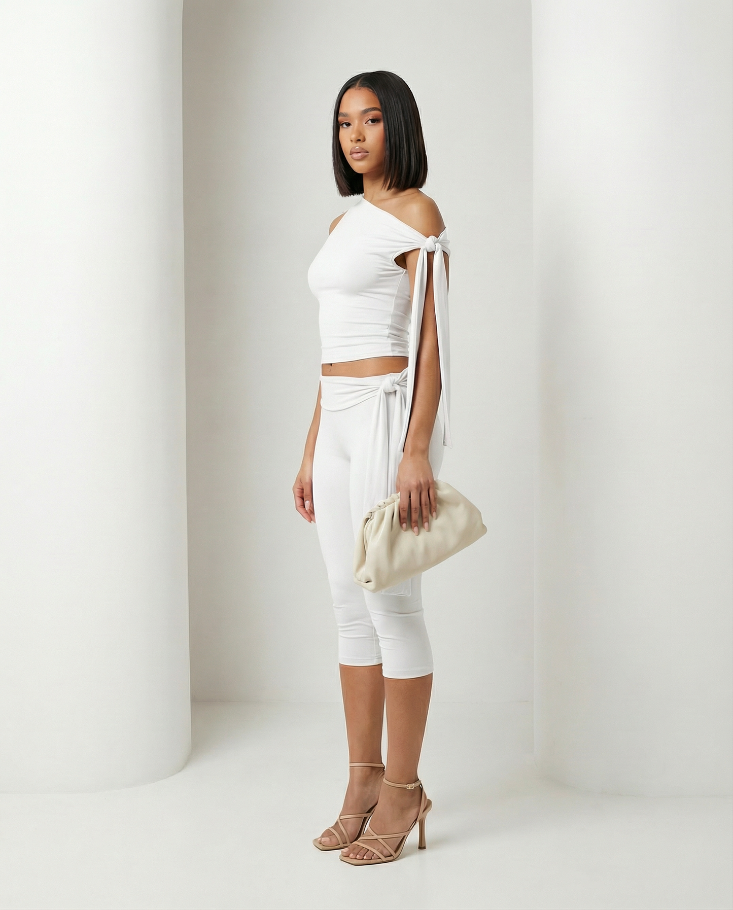White one-shoulder tie top and capri leggings seen from the side, showing the waist sash detail
