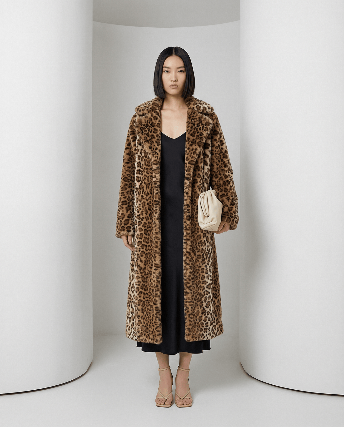 Cocoa leopard Aurelia coat open over a black slip dress with a cream clutch, full length