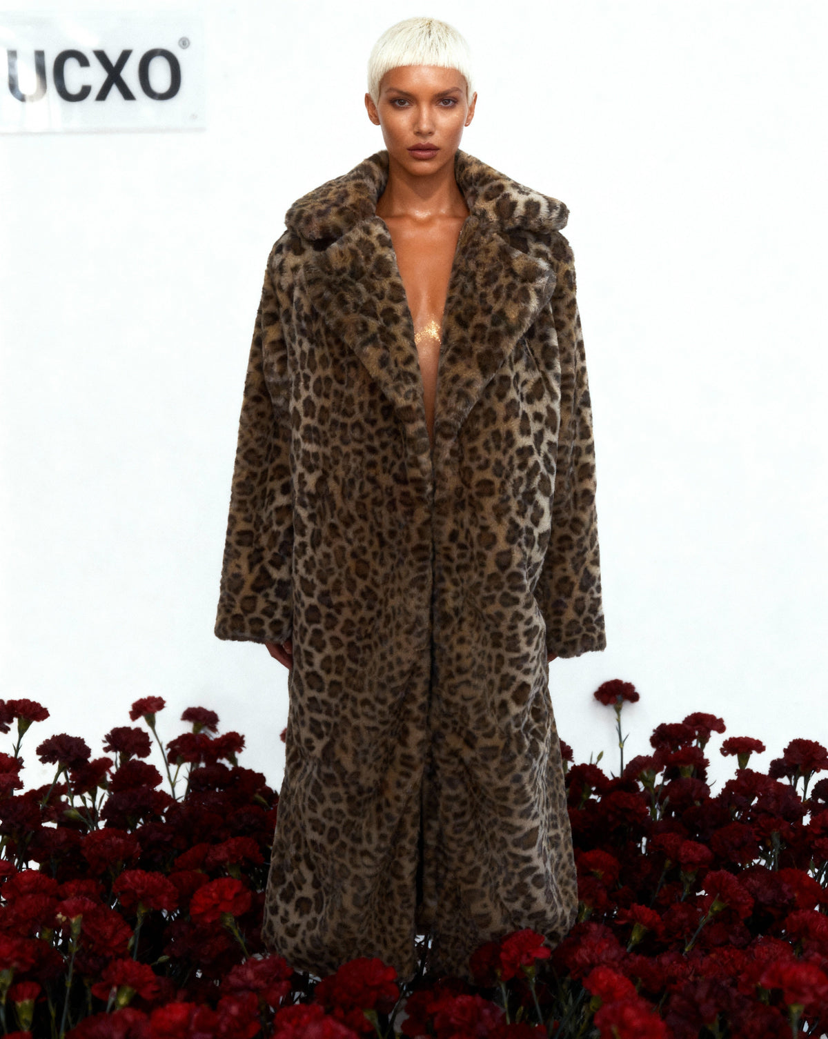 Leopard faux-fur coat worn open with a deep neckline, standing in dark red carnations