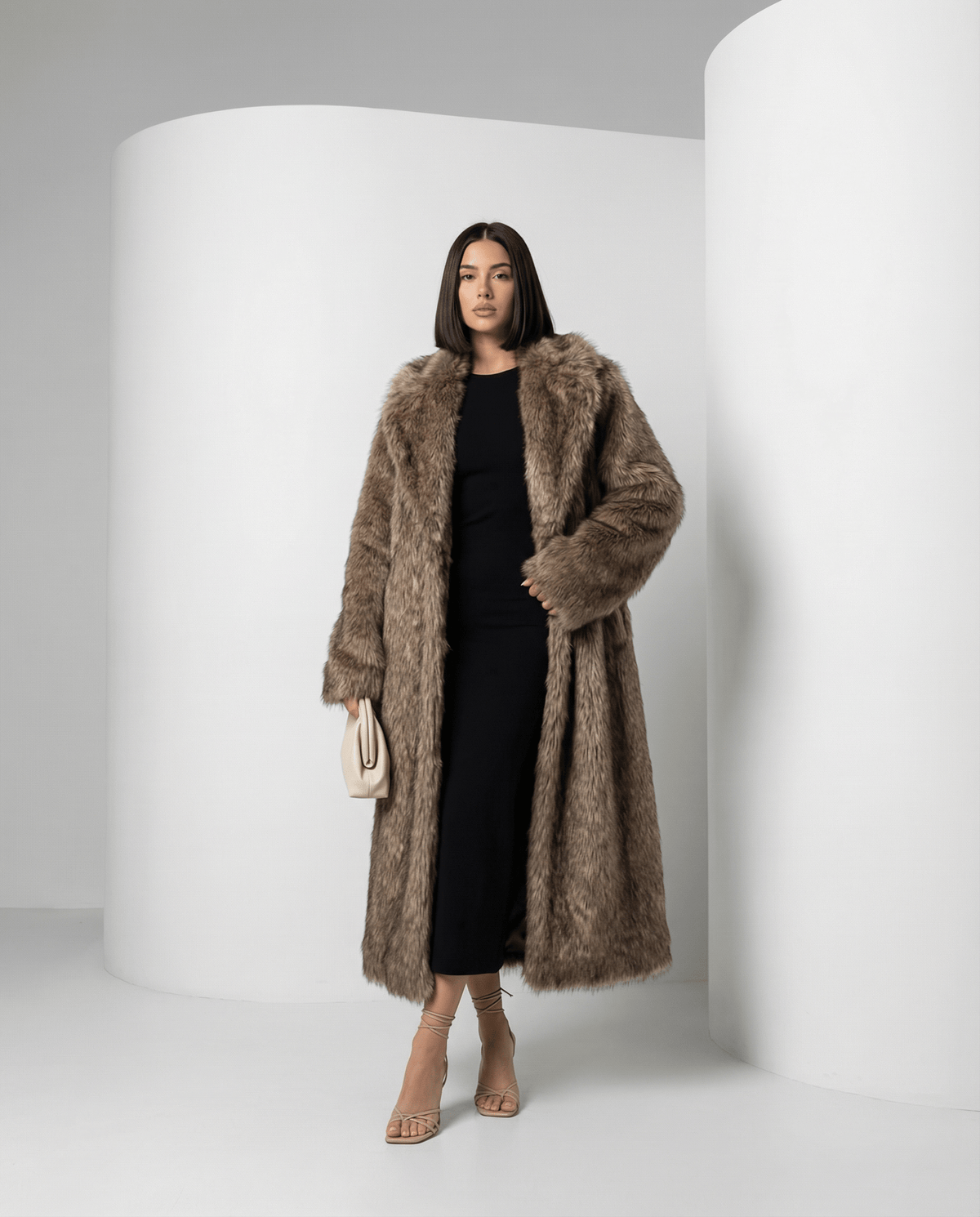 Beige longline faux-fur coat worn open with one hand in the pocket, angled stance, full length