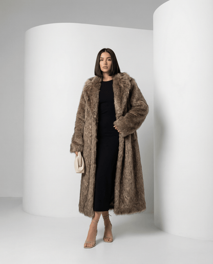 Beige longline faux-fur coat worn open with one hand in the pocket, angled stance, full length
