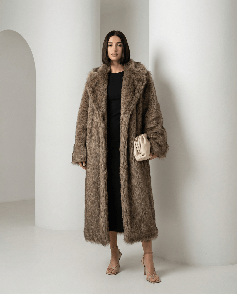Beige Eden longline faux-fur coat worn open over a black dress, full length beside a tan handbag