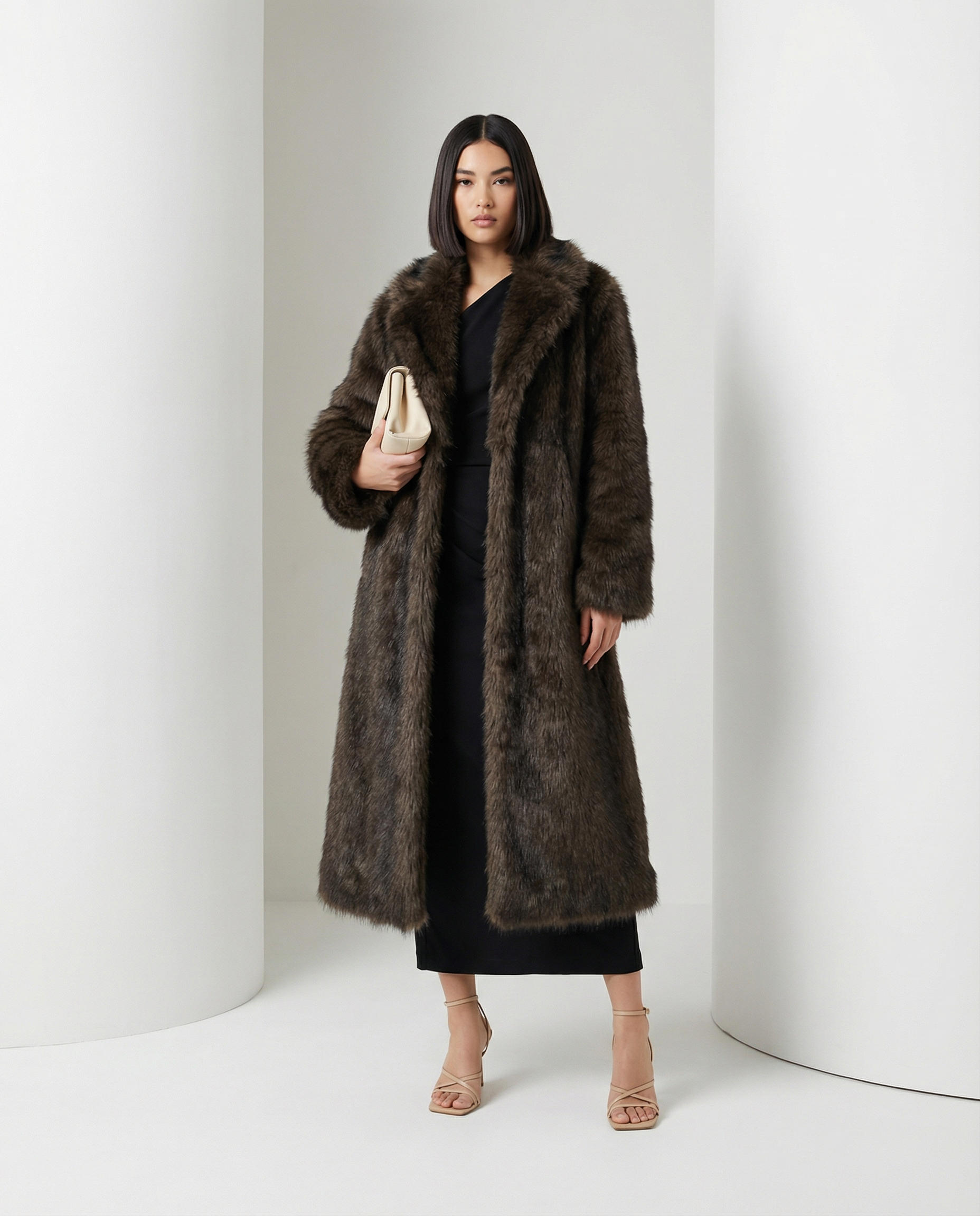 Brown Eden longline faux-fur coat worn open with a cream clutch held at the waist, full length