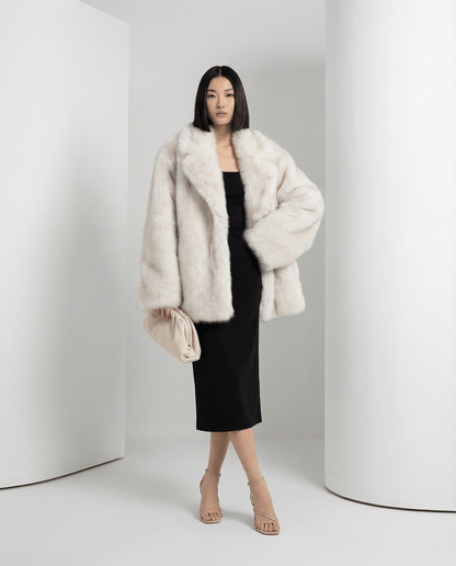 Frosted white oversized faux-fur coat worn open over a black midi dress, clutch under the arm