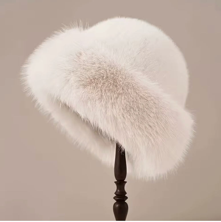 Cream faux fur bucket hat on a dark wooden stand against a soft beige studio backdrop