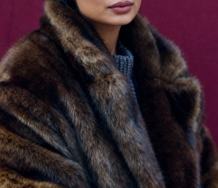 Tight crop of a brown faux fur coat's shawl collar against a deep burgundy wall