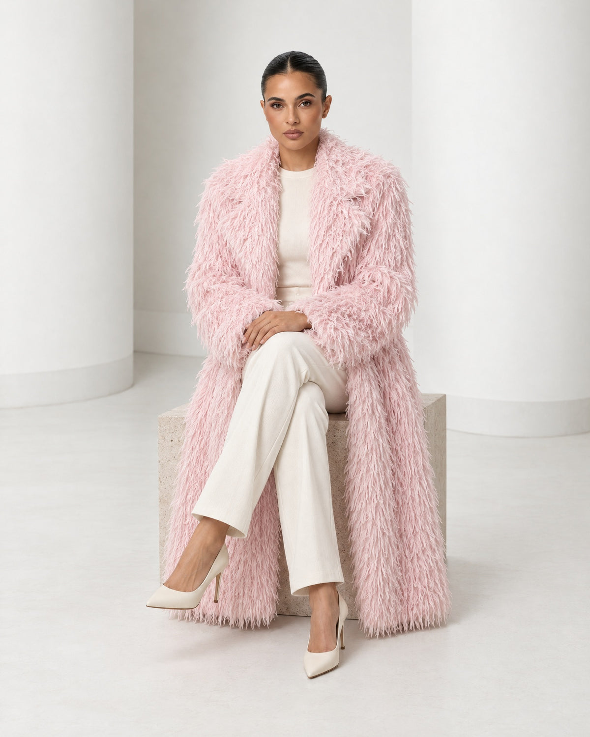 Freja coat in blush worn seated, falling open to the ankle over ivory trousers