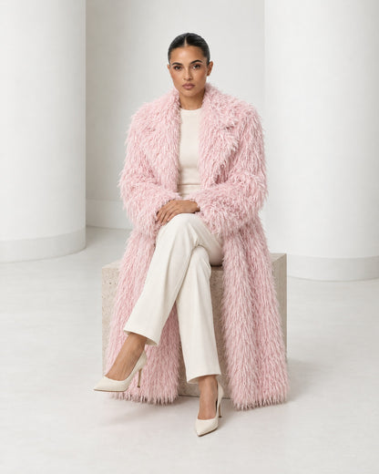 Freja coat in blush worn seated, falling open to the ankle over ivory trousers