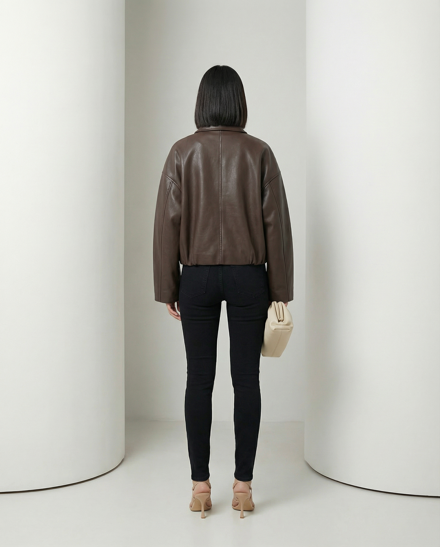 Back view of the brown cropped jacket showing the seamed yoke and belted hem over black jeans