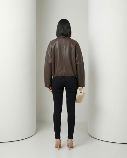 Back view of the brown cropped jacket showing the seamed yoke and belted hem over black jeans