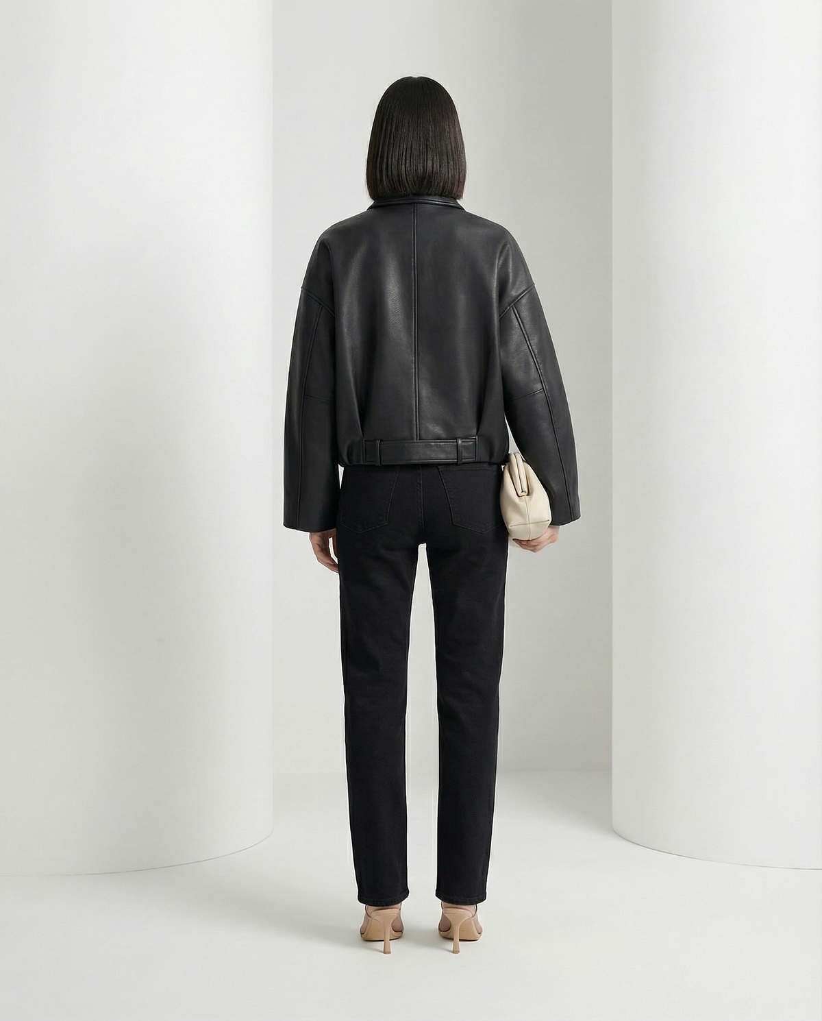 Back view of the black cropped jacket, belt buckled at the waist over straight black jeans