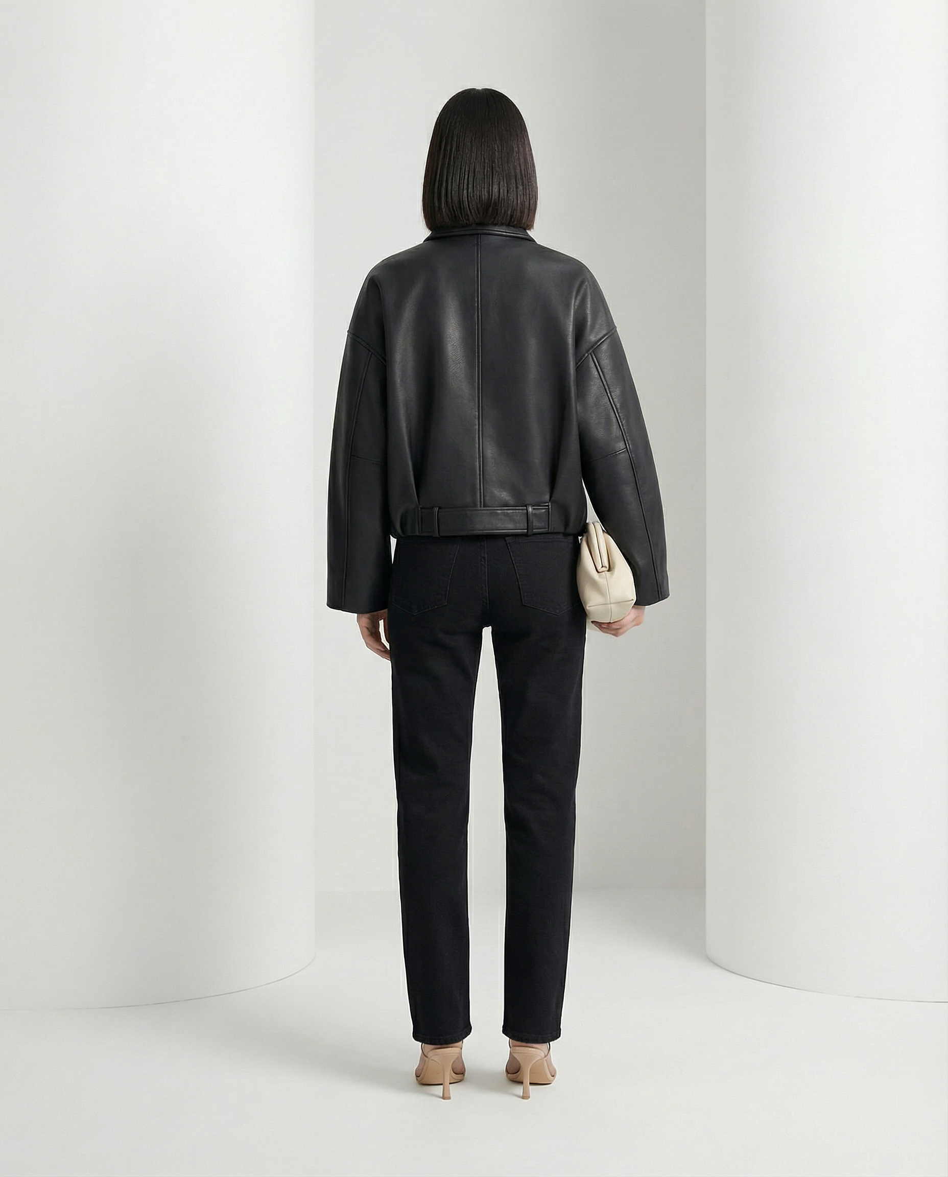 Back view of the black cropped jacket, belt buckled at the waist over straight black jeans
