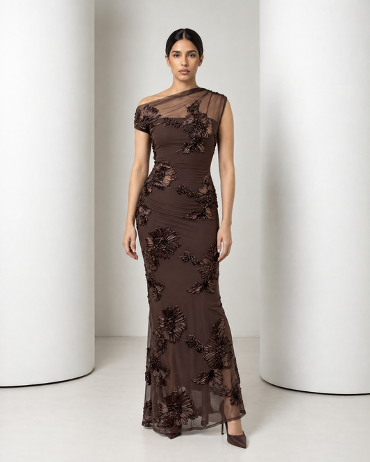 Model in the chocolate Maren gown, front view: sheer mesh yoke over one shoulder, raised floral appliqué, slim column skirt