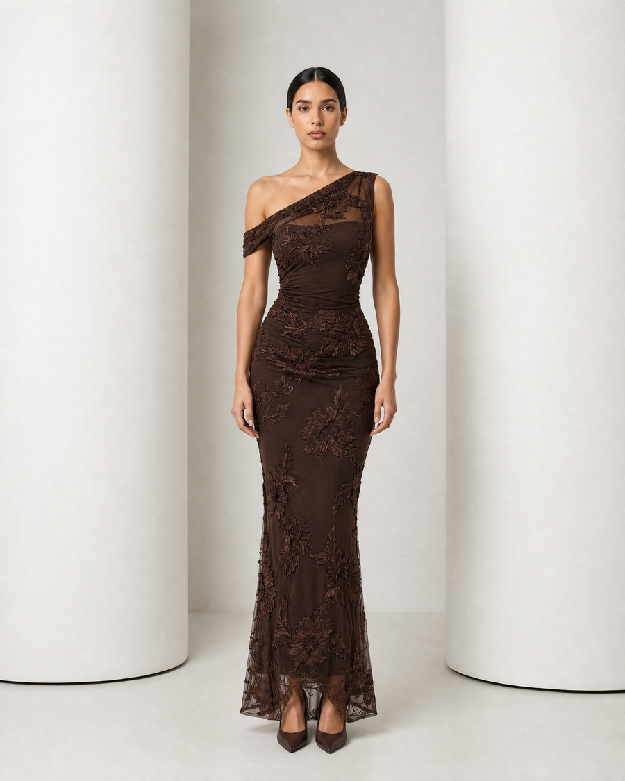 Model in the chocolate Maren gown, one draped shoulder, raised floral appliqué over sheer mesh
