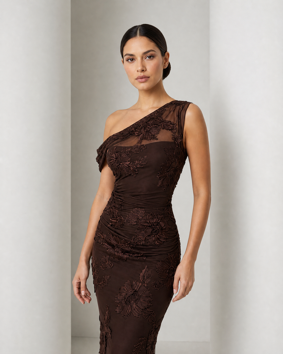 Model in the chocolate Maren gown, one draped shoulder, raised floral appliqué over sheer mesh