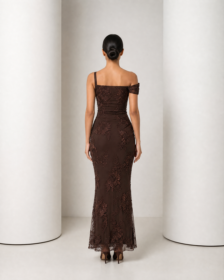 Model in the chocolate Maren gown, one draped shoulder, raised floral appliqué over sheer mesh