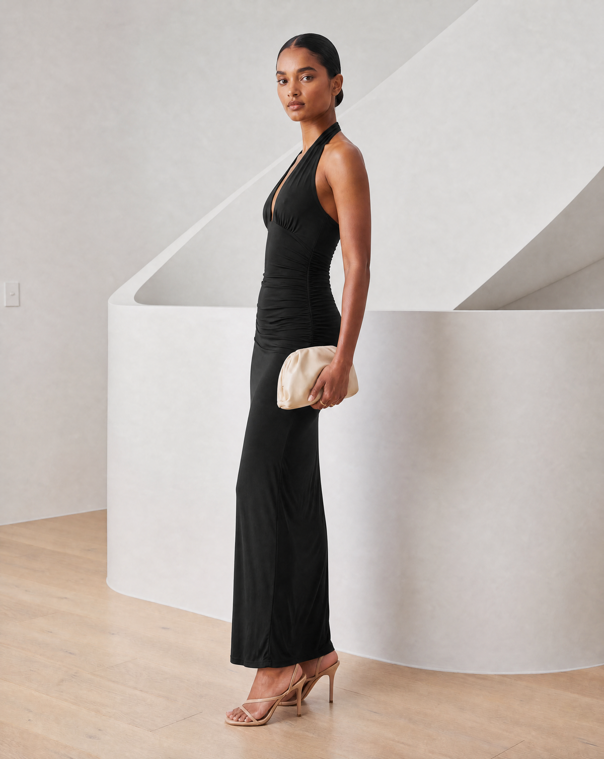 Meridiane halter maxi in black, side view with the model turned to camera holding a cream clutch