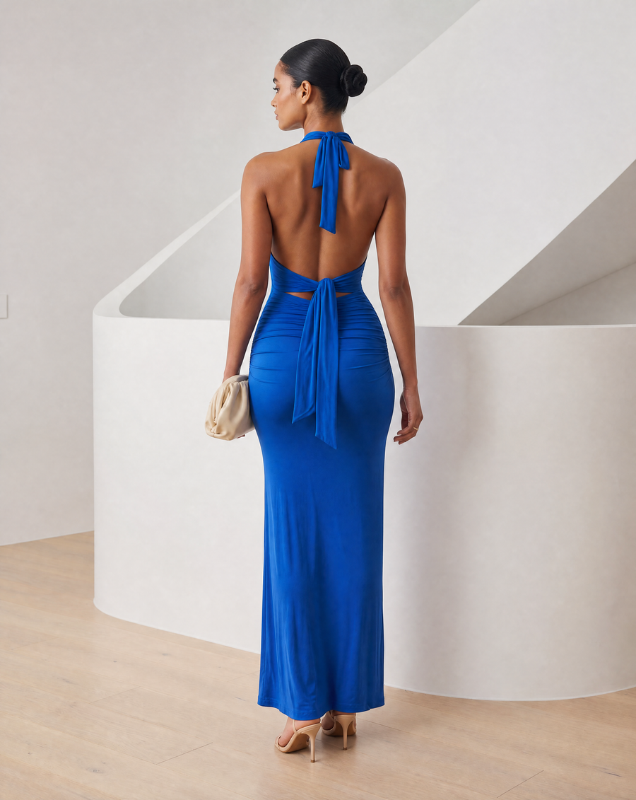 Cobalt blue Meridiane halter maxi dress worn with a cream clutch, full length front view