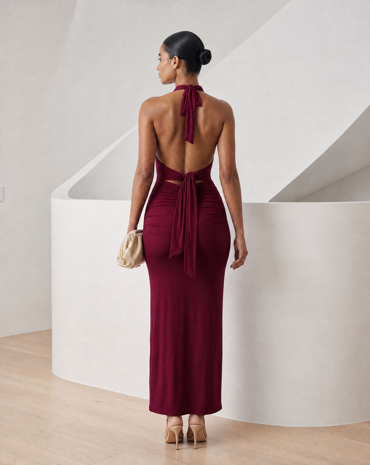 Burgundy halter maxi from behind with an open back, knotted sash and floor-length hem