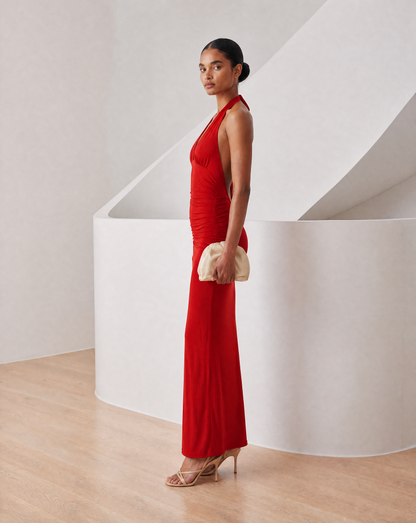 Meridiane halter maxi in true red, side view with the model glancing back over her shoulder