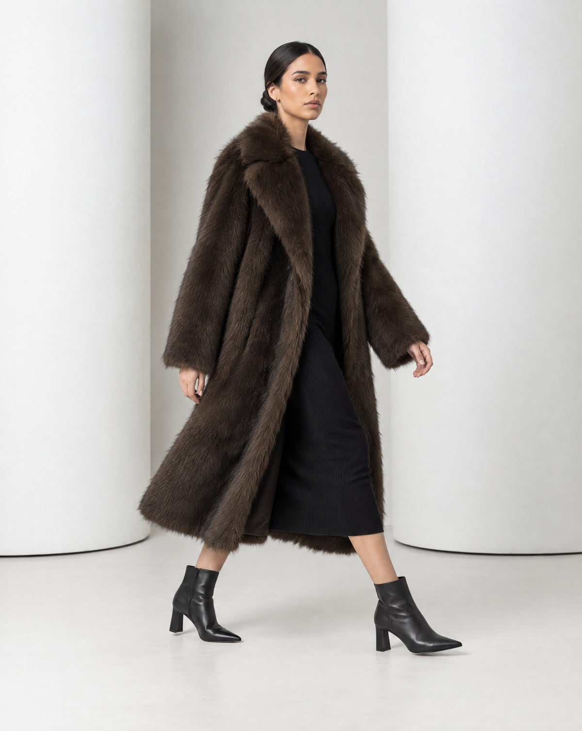 Side view of the Mirella bitter chocolate faux-fur coat mid-stride, the long open coat moving with the step