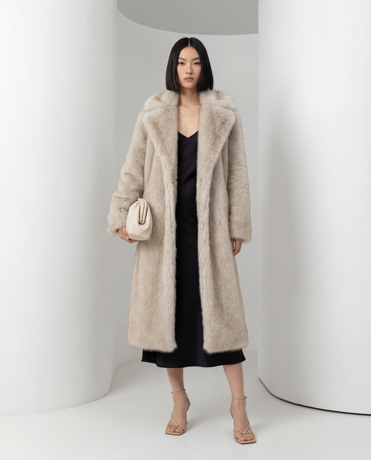 Beige faux-fur coat with a wide notch collar worn open, three-quarter view over a black slip dress
