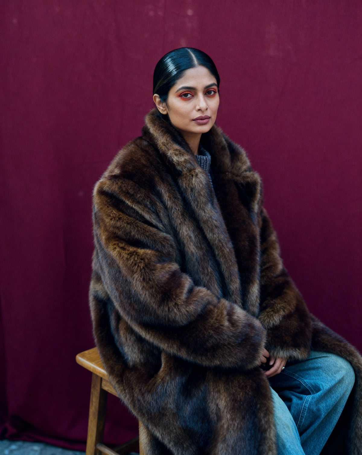 Bitter chocolate faux-fur coat with a deep collar, seated three-quarter view against a burgundy backdrop
