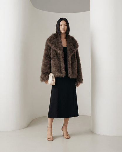 Cropped chocolate brown faux-fur jacket over a black midi dress, standing full length in a white studio