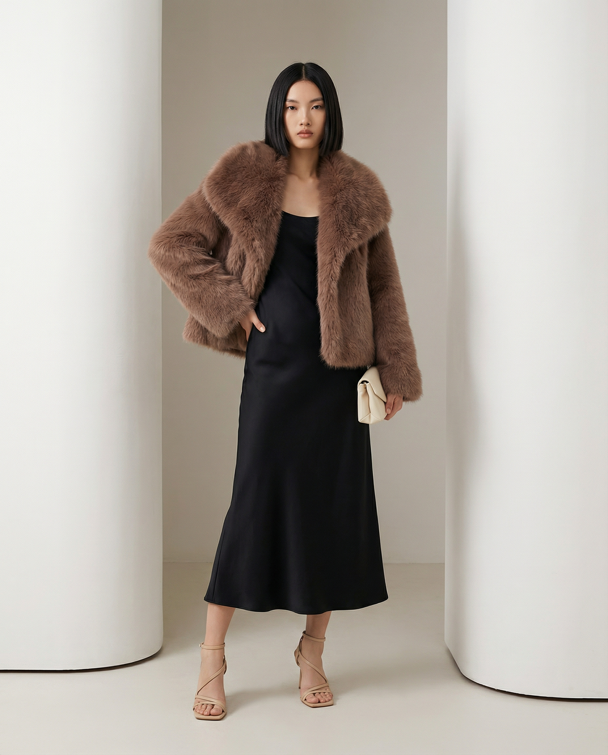 Cocoa brown cropped faux-fur jacket, one hand in the pocket, three-quarter view over a black dress
