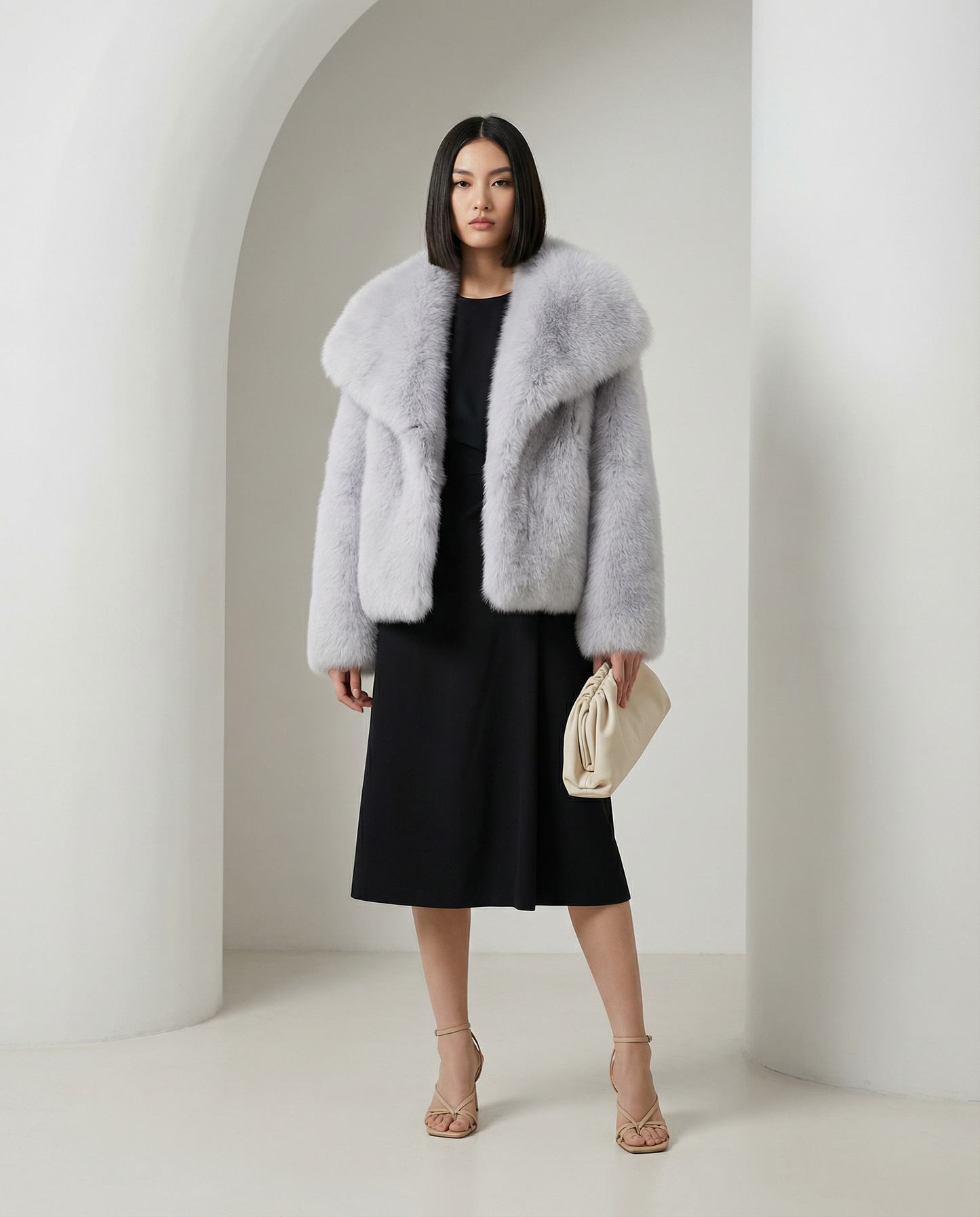 Pale silver-grey cropped faux-fur jacket under a white arch with a black midi dress and nude sandals