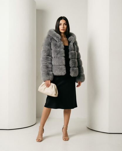 Grey faux-fur bubble jacket over a black slip midi dress, full length mid-step between white columns