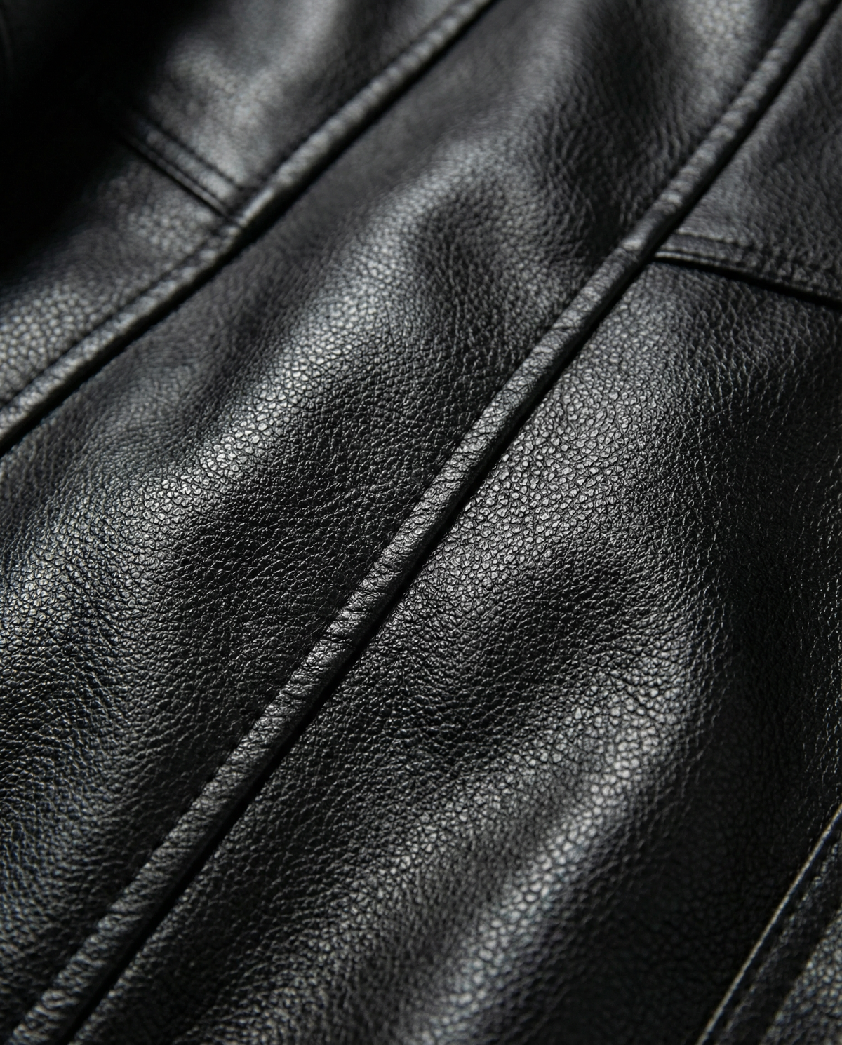 Macro shot of black pebbled leather, showing the grain and a topstitched panel seam