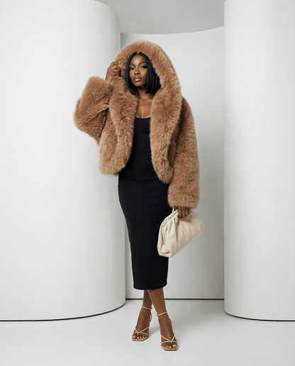 Amber fox Ravena hooded faux-fur jacket worn with the hood up over a black midi dress