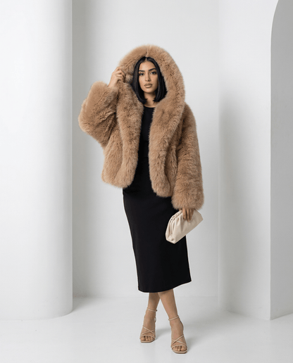 Amber fox hooded faux-fur jacket with the hood pulled up, three-quarter view with a cream clutch