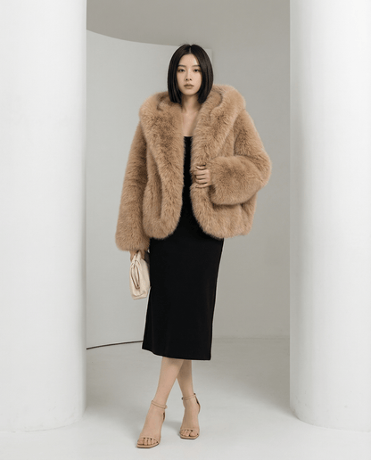 Amber fox cropped faux-fur jacket with a wide shawl hood, walking front view over a black midi dress