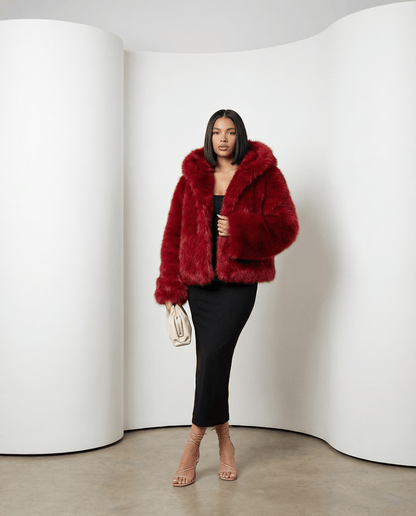 Ravena hooded faux-fur jacket in scarlet red, three-quarter view with hood down and cream clutch