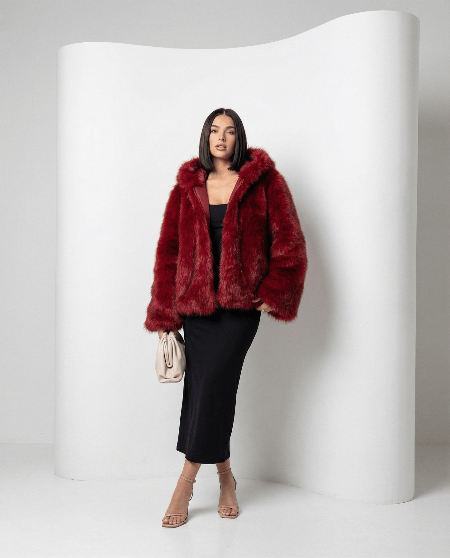 Scarlet red cropped faux-fur jacket with hood down, front view against a curved white studio wall