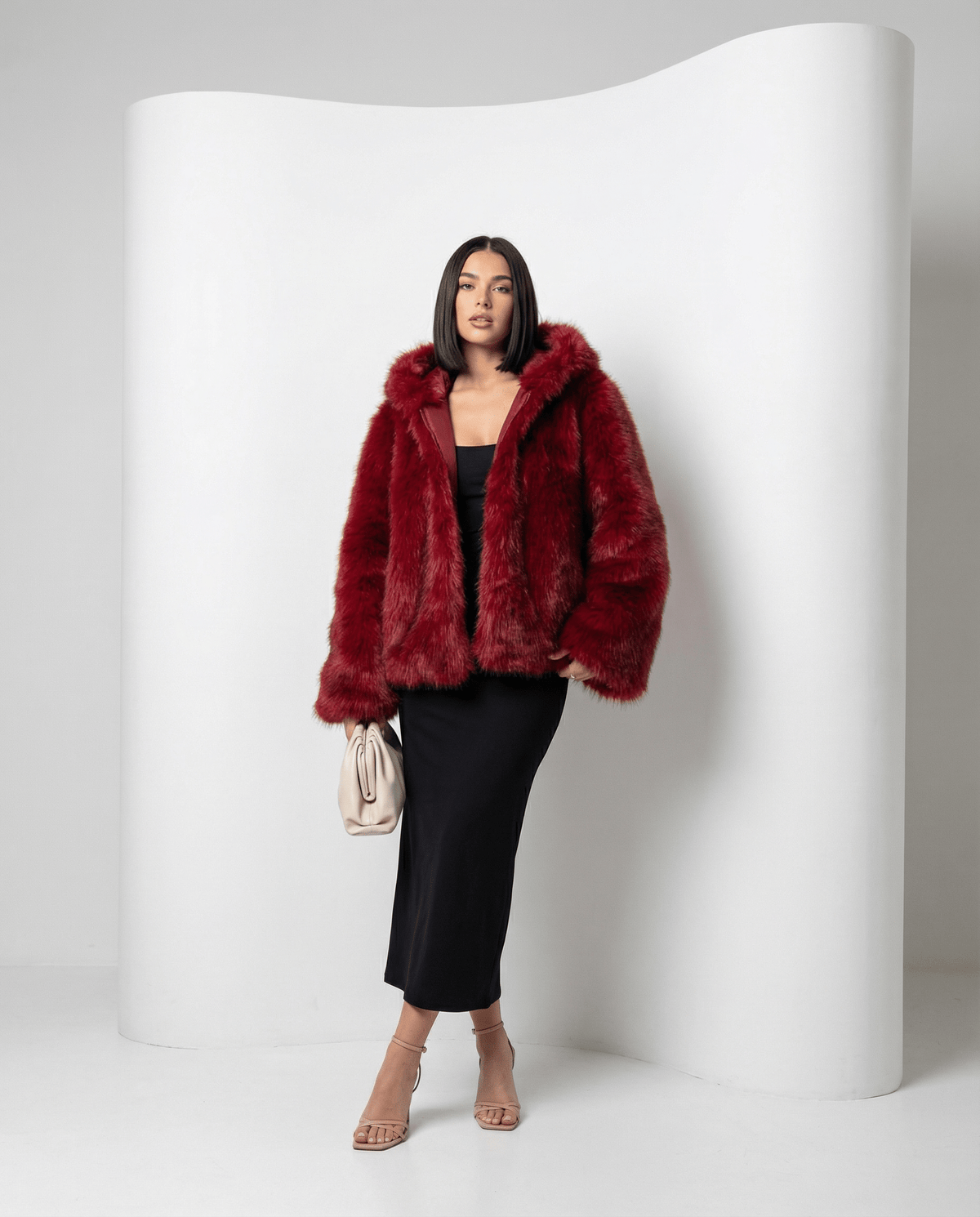 Scarlet red cropped faux-fur jacket with hood down, front view against a curved white studio wall