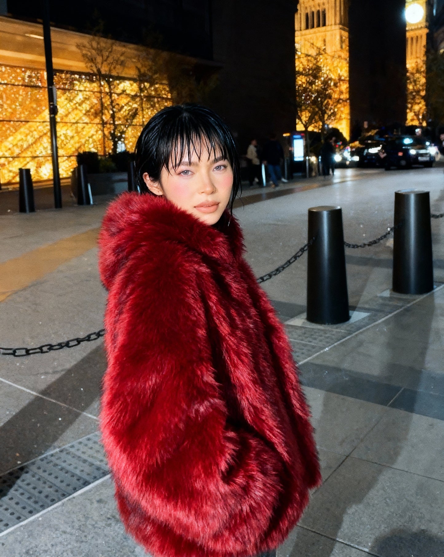 Scarlet red hooded faux-fur jacket seen from the side at night, hood down and collar turned up