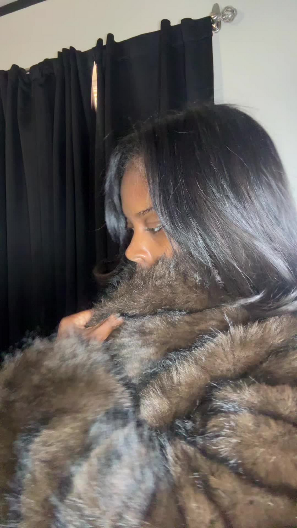 A customer resting her cheek against the collar of a brown and grey faux fur coat