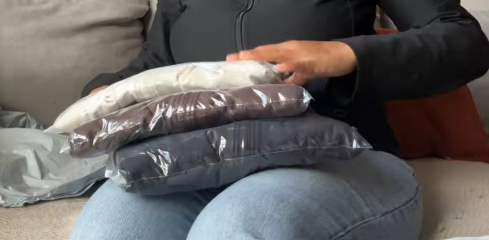 Three vacuum-sealed garment packs in cream, plum and grey stacked on a lap during unboxing