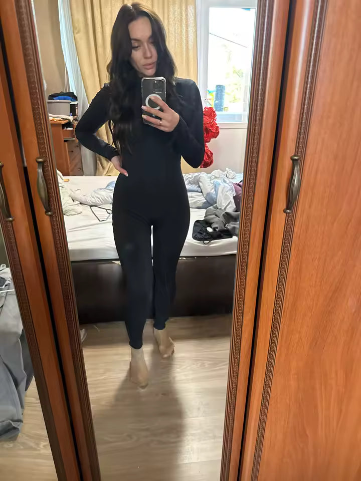 Black long-sleeve jumpsuit worn with nude heels, bedroom mirror selfie with a wardrobe door