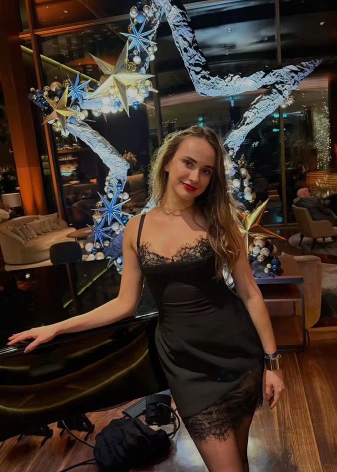 Black lace-trim slip dress worn at a lounge bar, with a lit star decoration behind