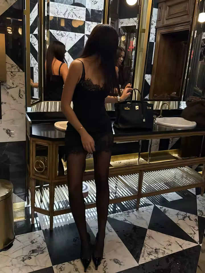 Back view of a black lace slip dress with sheer tights and heels in a marble powder room