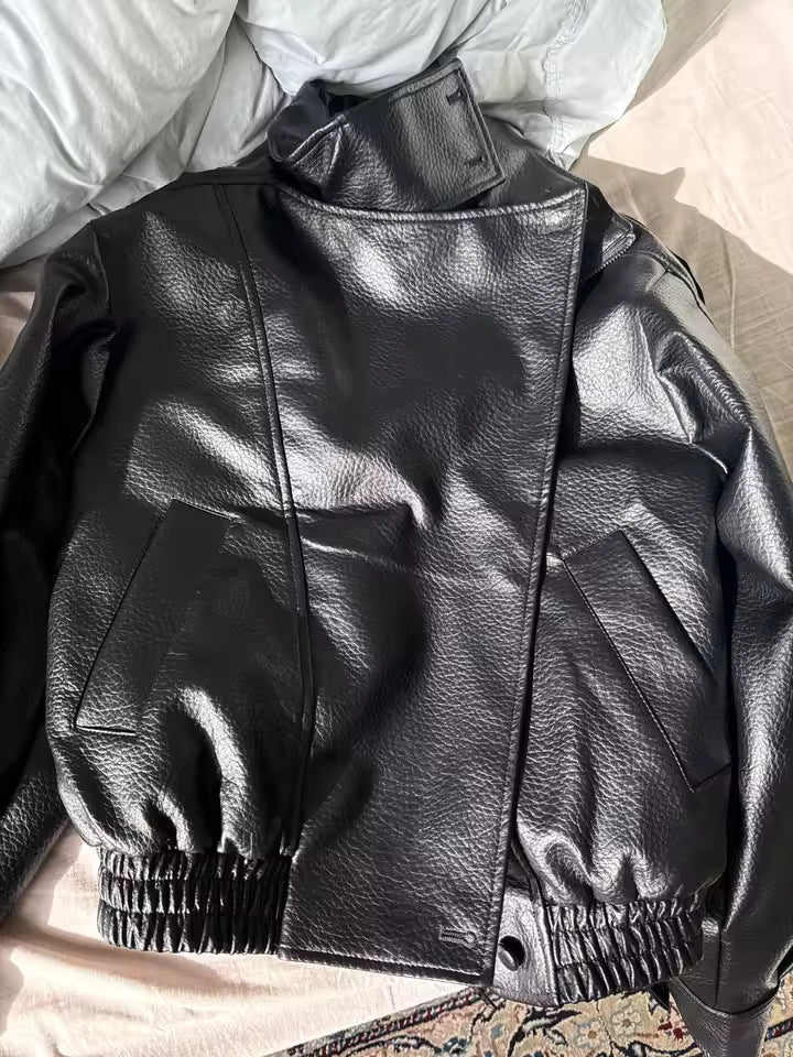 Black leather jacket with elasticated hem and patch pockets, laid flat on a bed