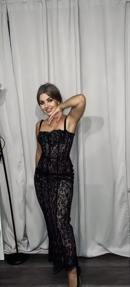 Sheer black lace maxi dress with a corset bodice, posed against pale curtains